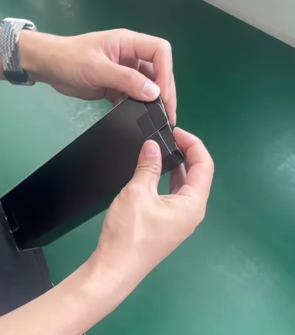 工場の作業台で、作業者の手が黒い化粧箱を組んでいる様子(白黒)